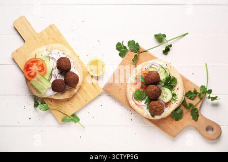 Cutting boards of delicious pitas with falafel and fresh vegetables on white wooden background Stock Photo