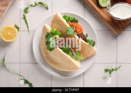 Plate of delicious pitas with falafel and fresh vegetables on white tile background Stock Photo