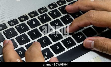 Laptop or computer keyboard with black keys and silver body. With his hands typing on the keyboard Stock Photo