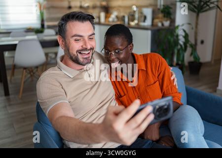 Playful Couple Taking a Selfie on the Couch at Home Stock Photo