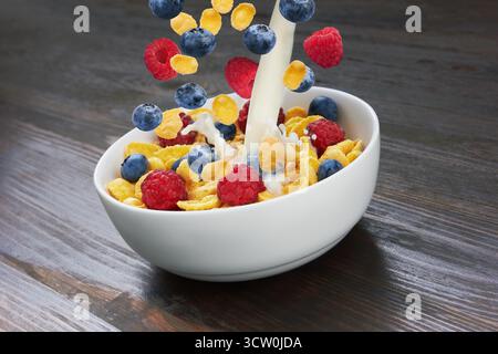 Falling corn flakes with fresh berries and pouring milk on wooden background Stock Photo