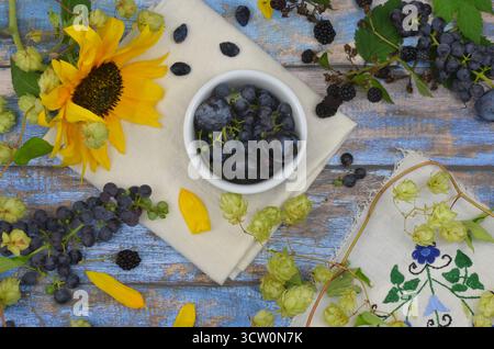 Plums, dark grapes and yellow sunflower on blue boards. Top view harvest from garden decorated with hop branches and Kashubian tablecloth. Stock Photo