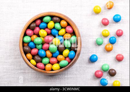 Colorful sugar-coated chocolate dragees, in a wooden bowl, on linen. Dragee chocolate confectionery. Stock Photo