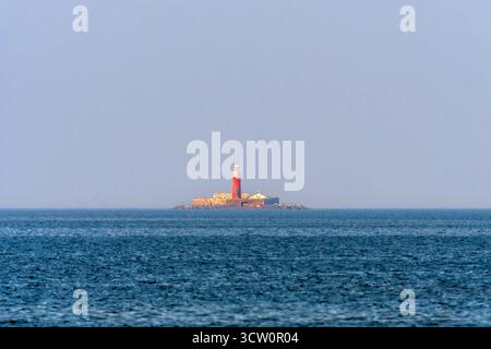 A lighthouse stands on a small, rocky island surrounded by blue water near Kolka, Latvia. Stock Photo