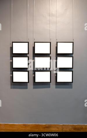 Six rectangular black frames with white centers are suspended from a gray wall with wood floor. Stock Photo