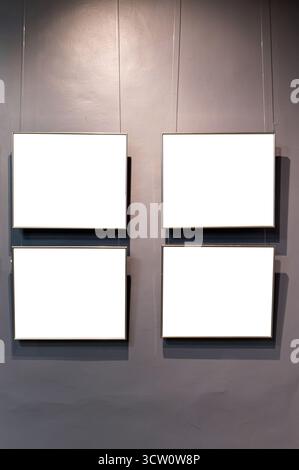 Four rectangular frames with white blank space hang on a grey wall by thin wires. Stock Photo