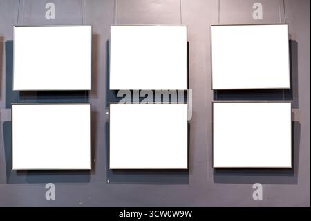 Six empty picture frames are displayed against a gray wall, hanging by clear wires. Stock Photo