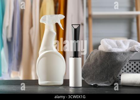Lint rollers, bottle of cleaning product and clothes on black table indoors Stock Photo