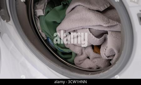 Authentic close-up of laundry inside a washing machine drum, showing towels and clothes before washing. Real-life concept of home chores, laundry care Stock Photo