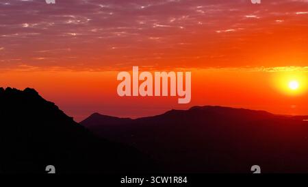 Aerial view of the sun setting over the dark silhouette of Table Mountain and the Cape Peninsula, the sky ablaze with fiery hues, Cape Town, Western Cape, South Africa. Stock Photo