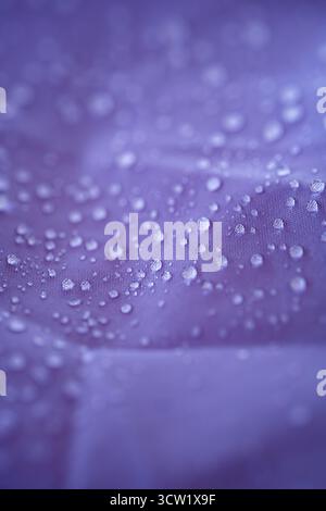 Water droplets on a waterproof or repellent purple textile fabric. Close up, macro shot, shallow depth of field, no people Stock Photo