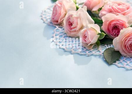 Flowers pink roses on openwork napkin on a blue paper background with space for text Stock Photo