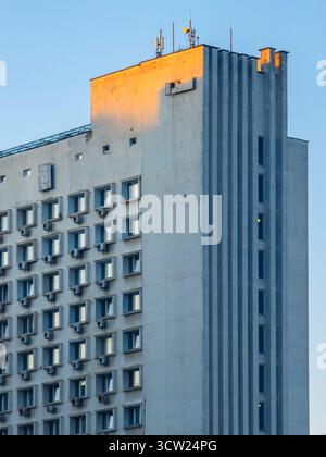 Brutalist concrete high rise facade with repeating windows and air conditioning units, rooftop antennas catching warm golden light against a clear coo Stock Photo