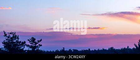 Evening sky displaying a colorful gradient from lavender to orange above a silhouetted forest line, creating a peaceful natural backdrop for abstract Stock Photo