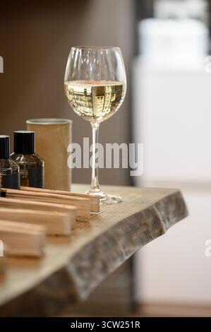 A glass of white wine on a wooden table next to incense sticks. Close up of wine on wooden shelf next to perfume in modern salon or store. Stock Photo