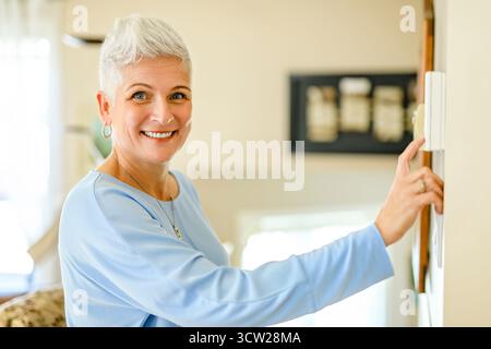 A Senior woam using Heating Thermostat At Home In Energy Crisis Stock Photo