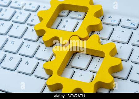 Yellow gear shapes on a computer keyboard symbolizing automation in computer systems, digital workflow, and technological process integration. Stock Photo