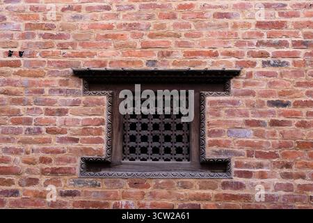Rustic red-brick wall with a carved wooden window and black lattice grille, showing weathered textures and historic charm Stock Photo