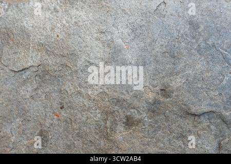 Close-up of a rough, weathered gray stone surface with cracks, natural imperfections, and subtle reddish-brown specks Stock Photo