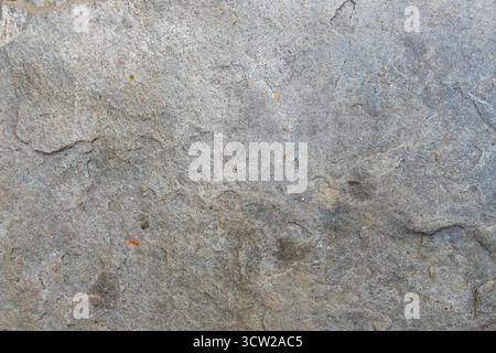 Close-up of a rough, weathered gray stone surface with cracks, natural imperfections, and subtle reddish-brown specks Stock Photo