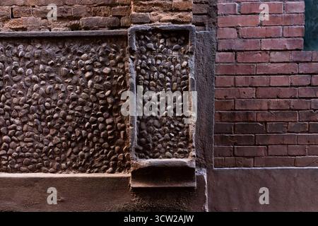 Urban street wall featuring a textured pebble panel and contrasting smooth and rough brick sections, showcasing rustic and modern textures. Stock Photo