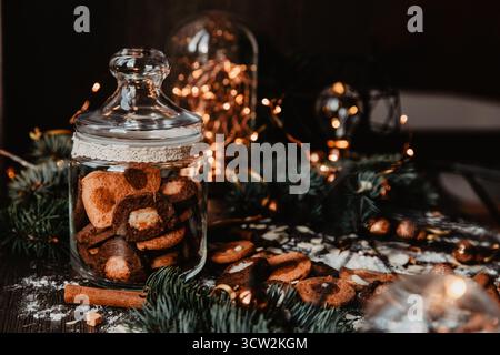 A rustic Christmas holiday setting featuring a jar of homemade cookies, surrounded by cinnamon sticks and festive lights. Stock Photo