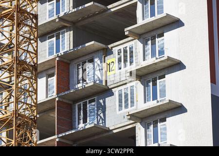 high-rise construction site features concrete floors with framed windows and a large number marking on one level. crane stands nearby under a clear sk Stock Photo