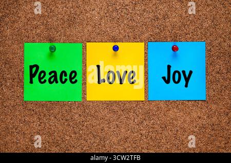 Three colored paper notes with words Peace, Love, Joy on a cork board Stock Photo