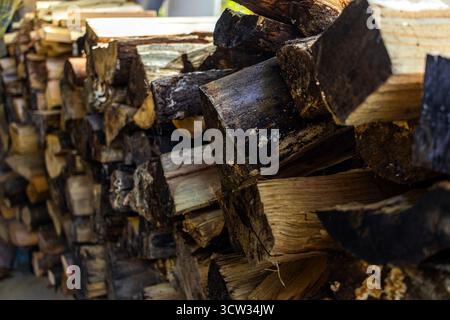 Stack of chopped firewood neatly piled on a porch, ready for use during the cold season. The wood shows a mix of fresh and seasoned logs. Stock Photo