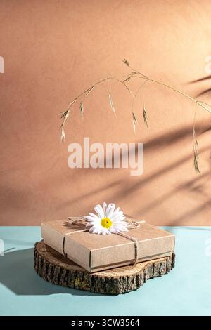 Craft gift box decorated with chamomile flower on a blue and orange background. Zero waste concept. copy space. Stock Photo