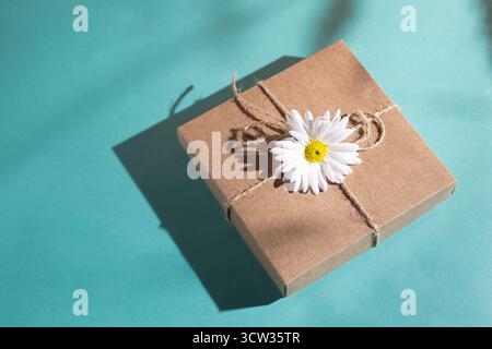 Craft gift box decorated with chamomile flower on a blue background. Stock Photo