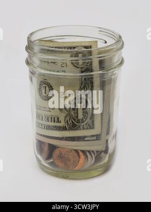 A small tip jar, filled with U.S. dollars and cents, is shown isolated, set against a white background. Stock Photo