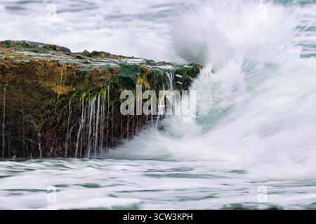 Background with ocean waves breaking on rocks covered with seaweed at Agua Amarga beach, Alicante, Spain Stock Photo