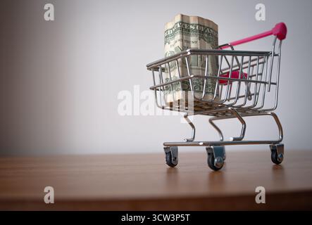 A sharp, eye-catching close-up features a miniature shopping cart with a distinct pink handle, entirely filled to the brim with one-dollar bills. Plac Stock Photo