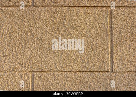 Beige brick wall with rough plaster texture in warm sunlight. Architectural background showing decorative facade pattern and structure detail. Stock Photo