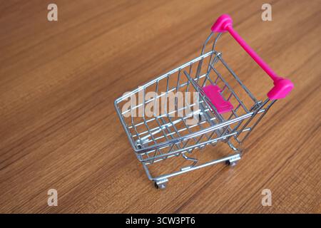 A clean, focused shot features a miniature, empty grocery shopping cart trolley positioned centrally on a smooth wooden surface Stock Photo