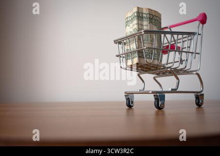 A sharp, eye-catching close-up features a miniature shopping cart with a distinct pink handle, entirely filled to the brim with one-dollar bills Stock Photo