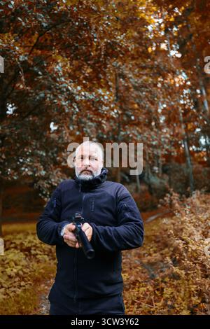 Bearded man in black jacket with gun, security concept in nature setting. copy space Stock Photo