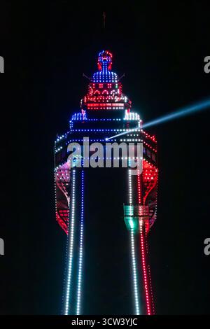 close up of the top of blackpool tower at night illuminated by red and blue lights and shining a beam of light into the black night sky Stock Photo