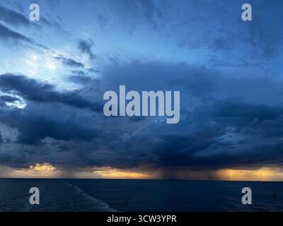 Dramatic rainstorm over the open sea near Le Havre, France, with dark storm clouds and sunlight breaking through the horizon. Stock Photo