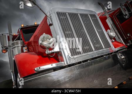 Two classic red trucks stand parked against a dark, cloudy sky, showcasing their shiny chrome details and powerful design during a moody afternoon. Stock Photo