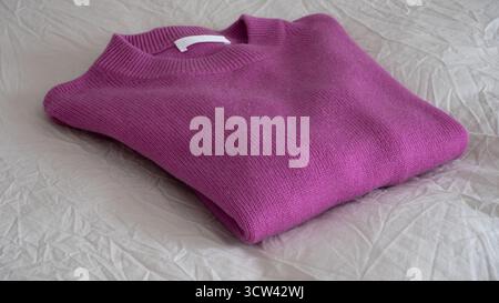 Minimalistic photo of a neatly folded pink cashmere sweater lying on a light, wrinkled textile background. Cozy and elegant concept, ideal for illustr Stock Photo