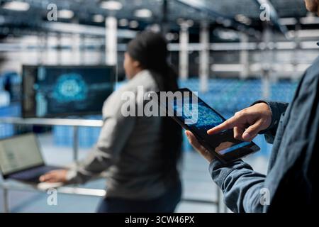 Close up of computer scientist in server hub using tablet to enhance AI model accuracy. Data center software developer using device to schedule maintenance for AI hardware rigs Stock Photo