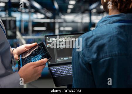 Close up of IT specialists on industrial platform collaborating on servers maintenance with artificial intelligence. Engineers team supporting infrastructure AI machine learning automatization. Stock Photo