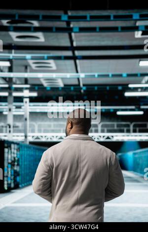 Computer scientist walking in server farm, overseeing mainframes gear used for managing databases. IT specialist in high tech data center doing checkup on rackmounts storing information Stock Photo
