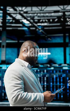 Server hub admin checking recovery plan on tablet, tracking resource utilization trends. Data center IT expert scanning hardware logs for faults, making sure rigs are functioning optimally Stock Photo