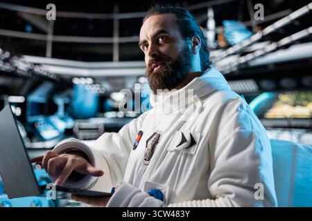 Astronaut doing galaxy observation using laptop dashboard displaying solar metrics in spacecraft. Spaceship crew member in spacesuit looking at orbital path on notebook during planetary exploration Stock Photo