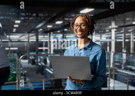 Portrait of black smiling technician monitoring AI LLM visualization on industrial platform in server hub, neural network systems. Female engineer brainstorming ideas for development. Stock Photo