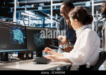 Data center system administrators using computer to visualize artificial intelligence neural networks made up of interconnected nodes. Server hub coworkers doing brainstorming, overseeing AI systems Stock Photo