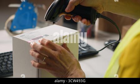Asian employee applying shipping labels and scanning tracking info, registering the cargo information for parcel status during delivery. Manages labeling tasks with hi vis vest in depot. Camera B. Stock Photo